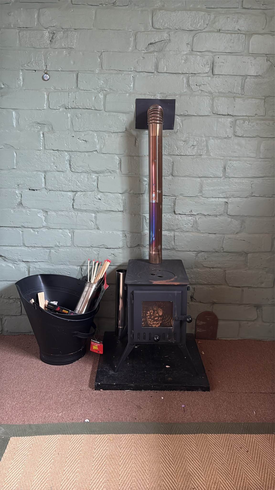 The little wood burner with its copper flue against the sage-painted wall